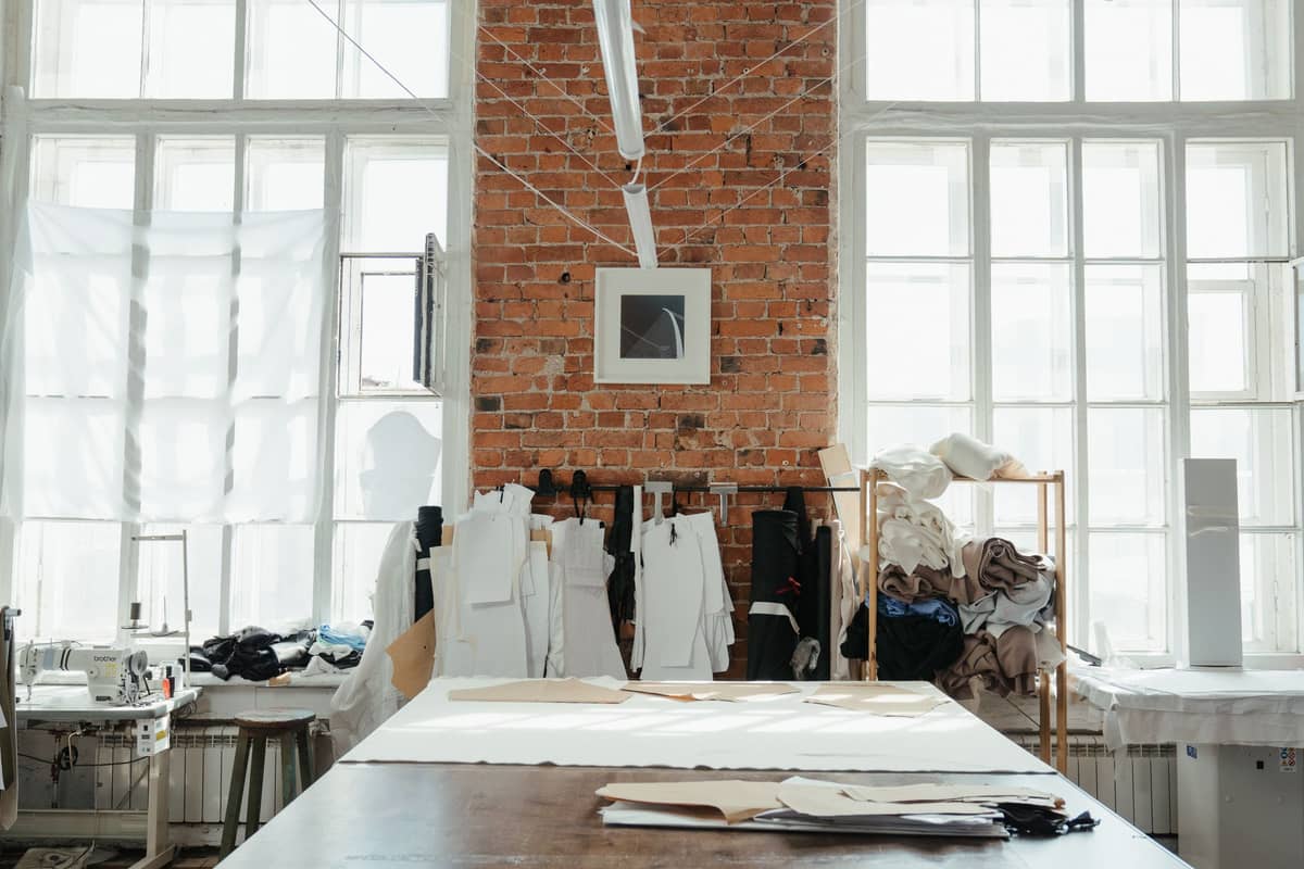 A bright atelier with tall windows, cutting tables and pattern rails