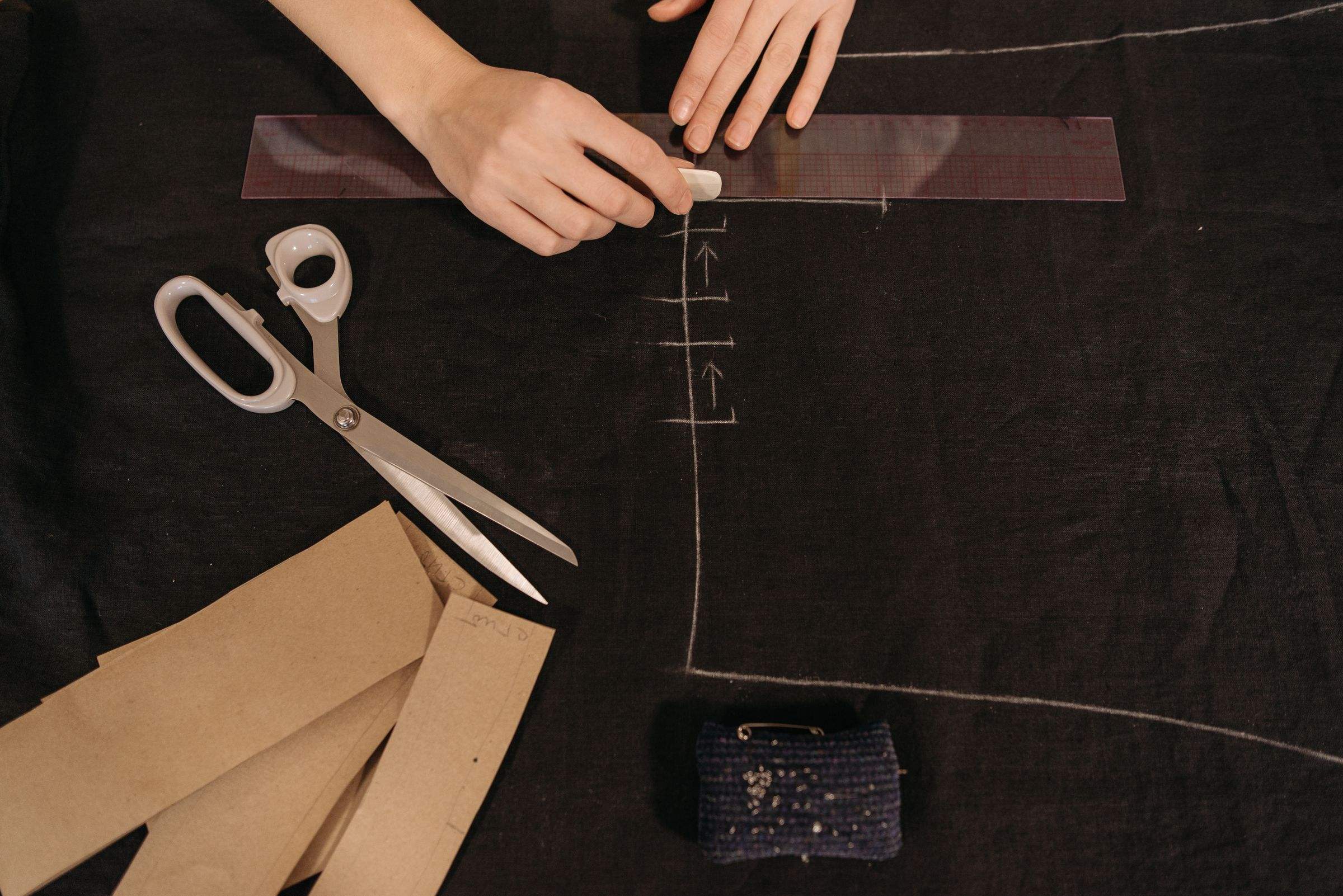 Chalk-marking black fabric against a ruler, with shears and pattern pieces