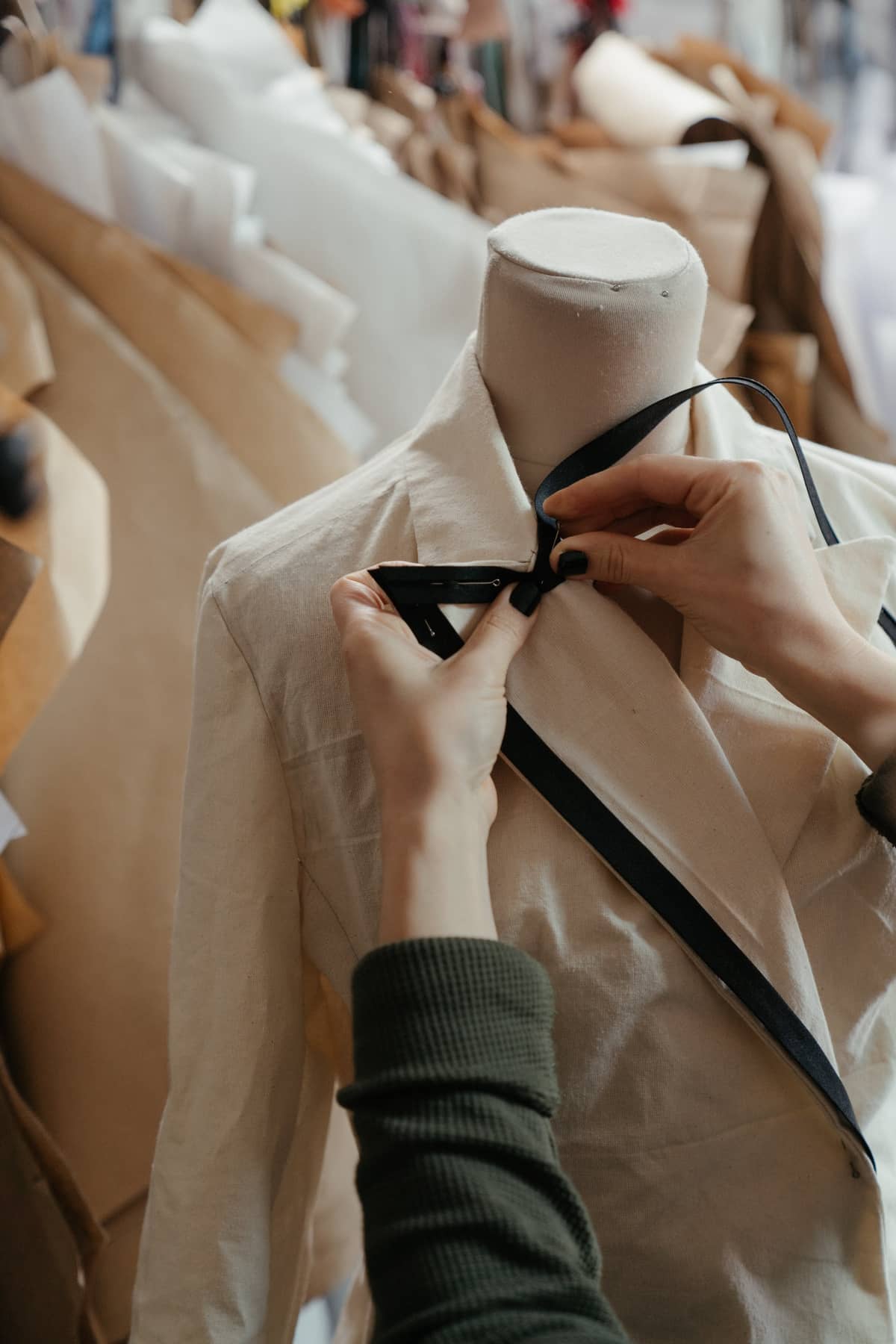 Pinning black bias tape onto a muslin jacket on a dress form