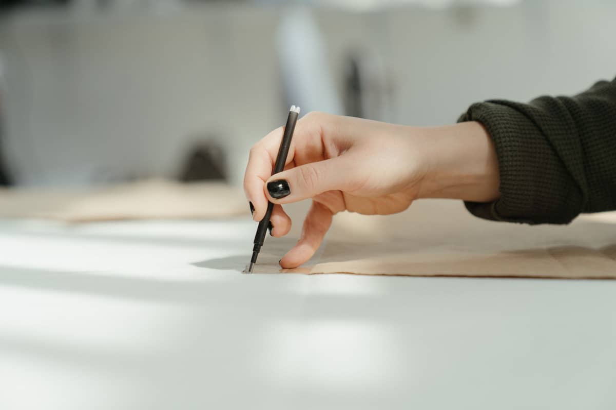 A hand drafting a pattern line on a sunlit cutting table
