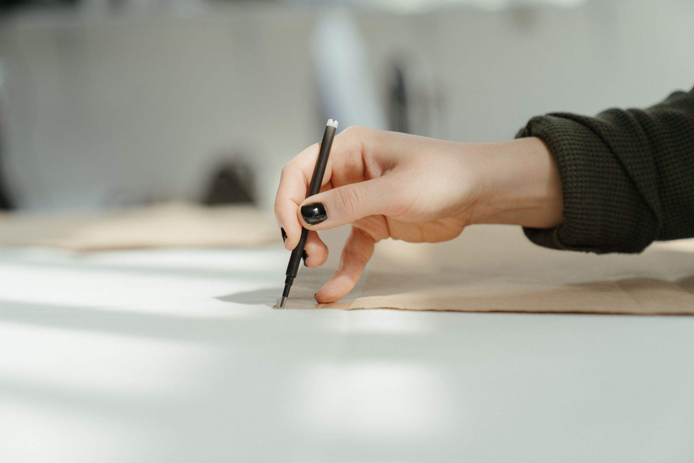 A hand drafting a pattern line on a sunlit cutting table