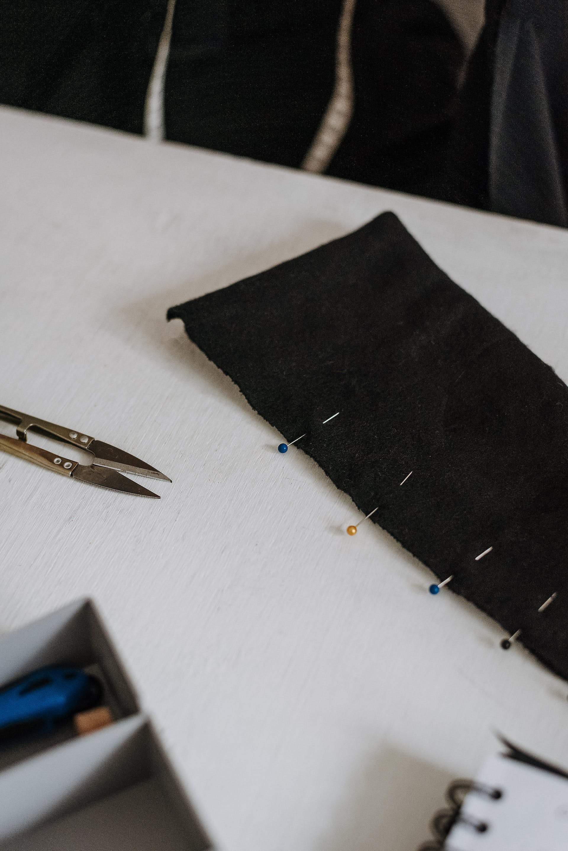Coloured pins along the edge of black fabric beside thread snips