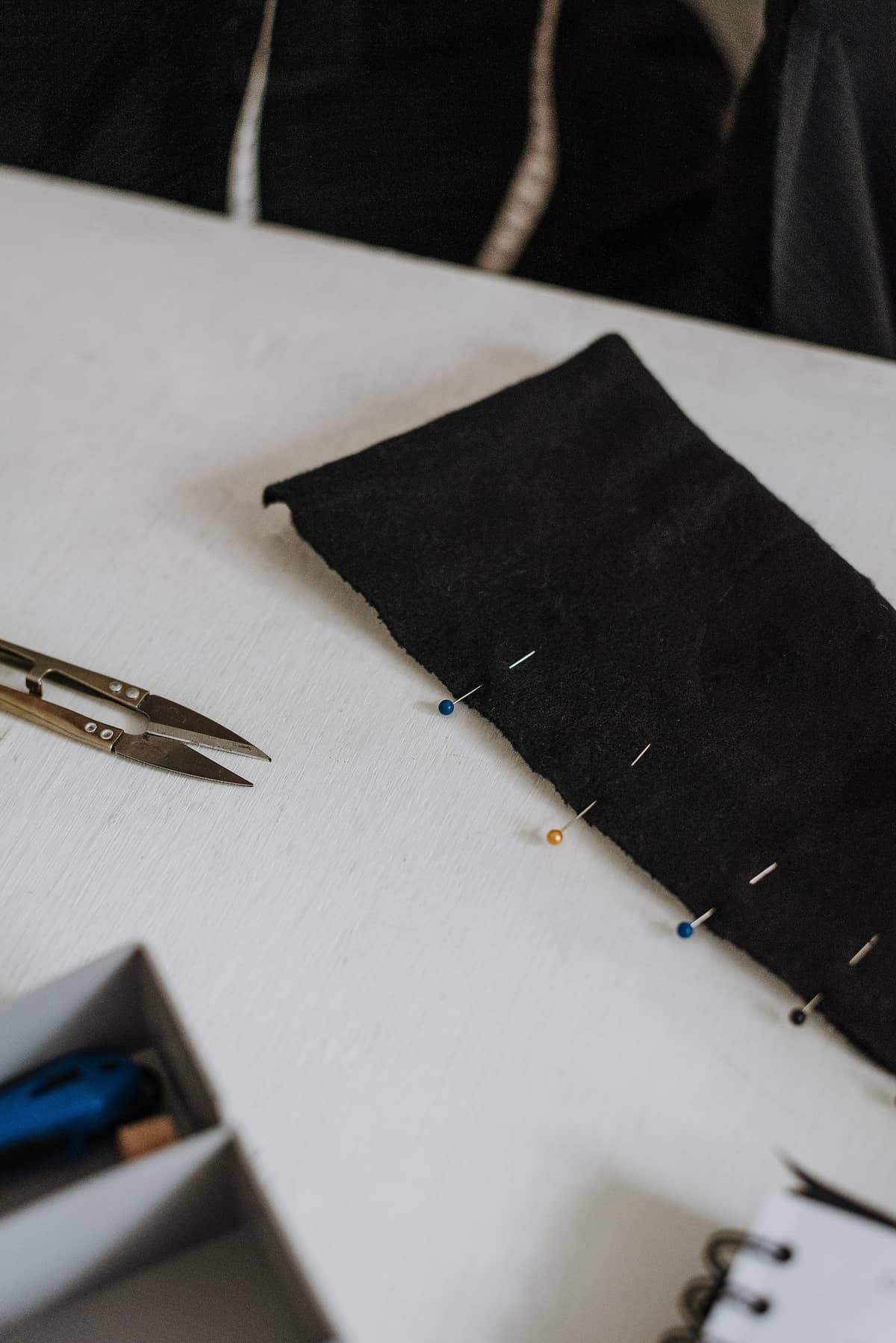 Coloured pins along the edge of black fabric beside thread snips